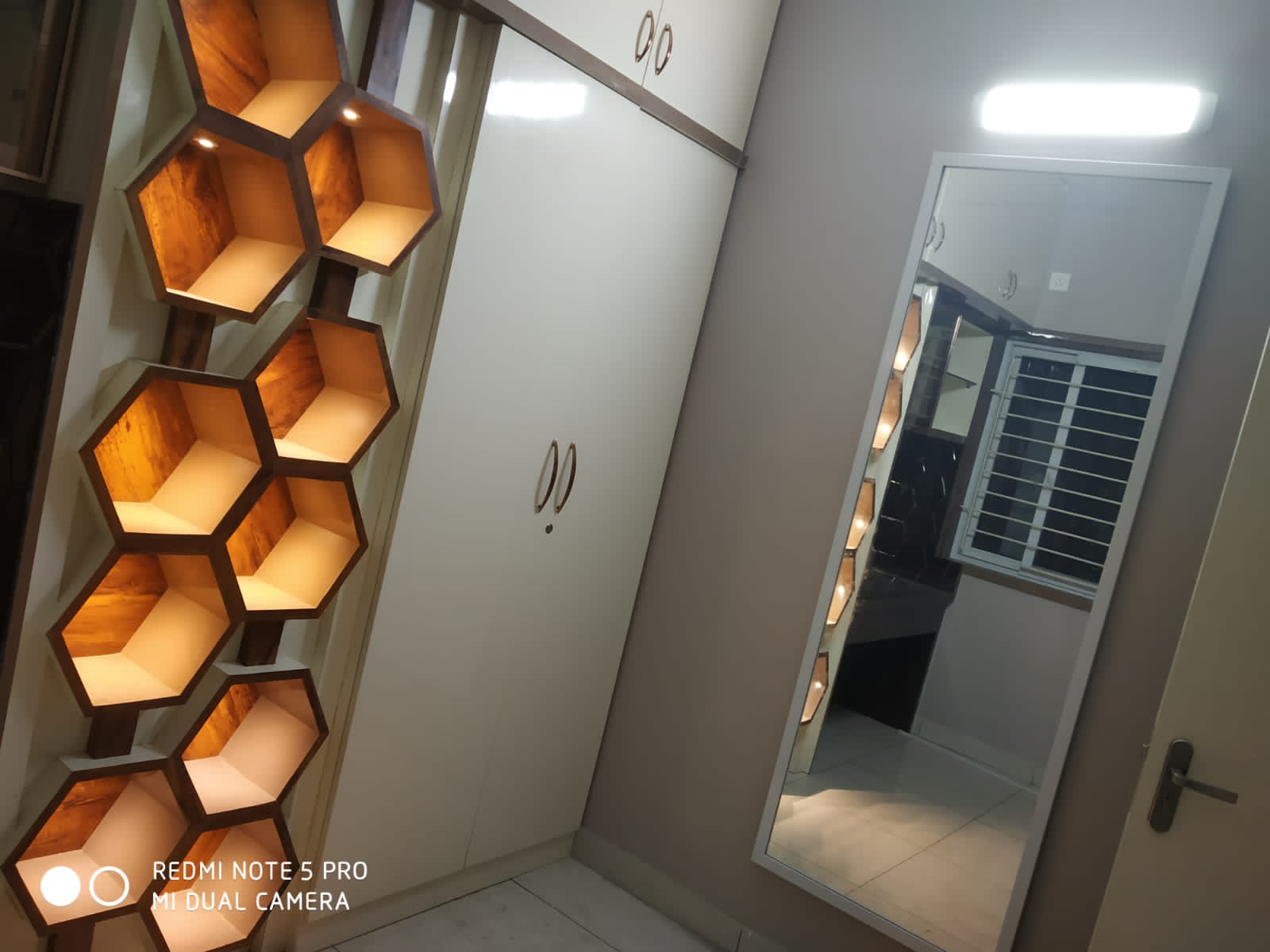 Umer's Residence, Bengaluru — Backlit honeycomb display shelving beside a white glossy wardrobe and full-length mirror