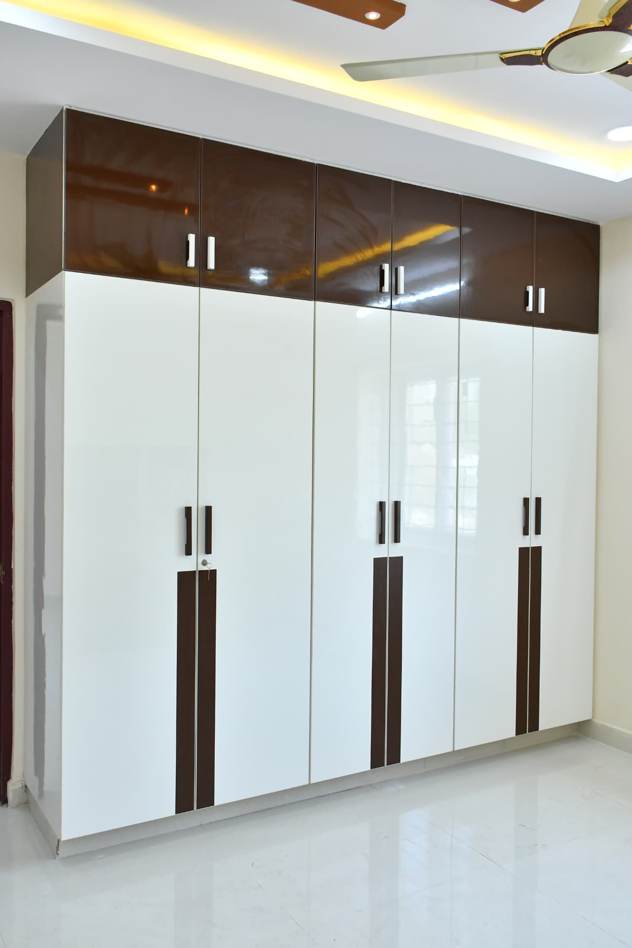 Mrs. Vasundara's Residence, Ballari — Six-shutter wardrobe with loft storage in high-gloss white and brown