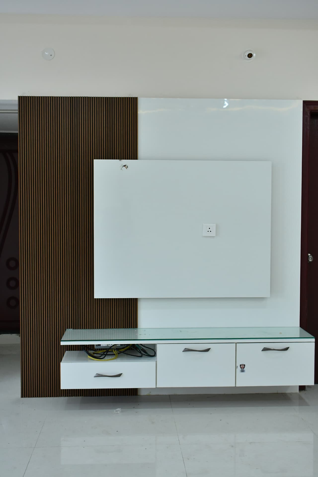 Mrs. Vasundara's Residence, Ballari — TV unit with fluted wood panel, glossy white back panel and glass-topped storage