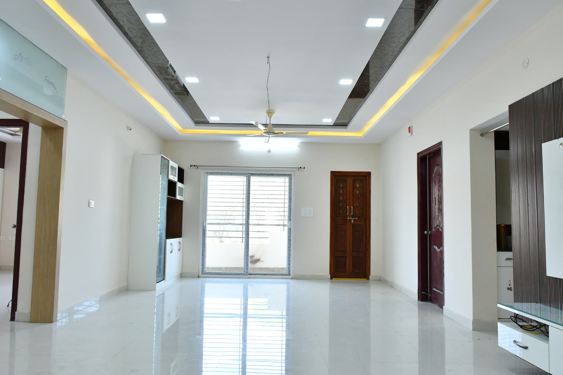 Mrs. Vasundara's Residence, Ballari — Open living and dining view with crockery unit, fluted TV panel and teak main door