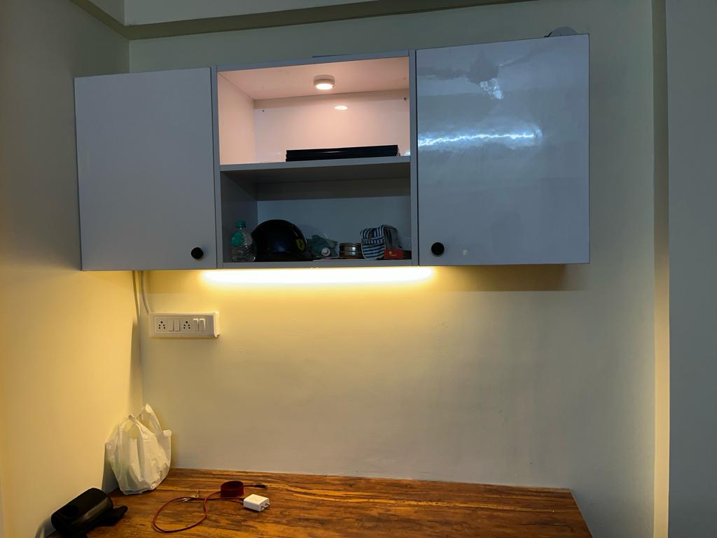 Rohan's Flat, Bangalore — Wall-mounted glossy overhead storage with under-cabinet lighting over a teak desk