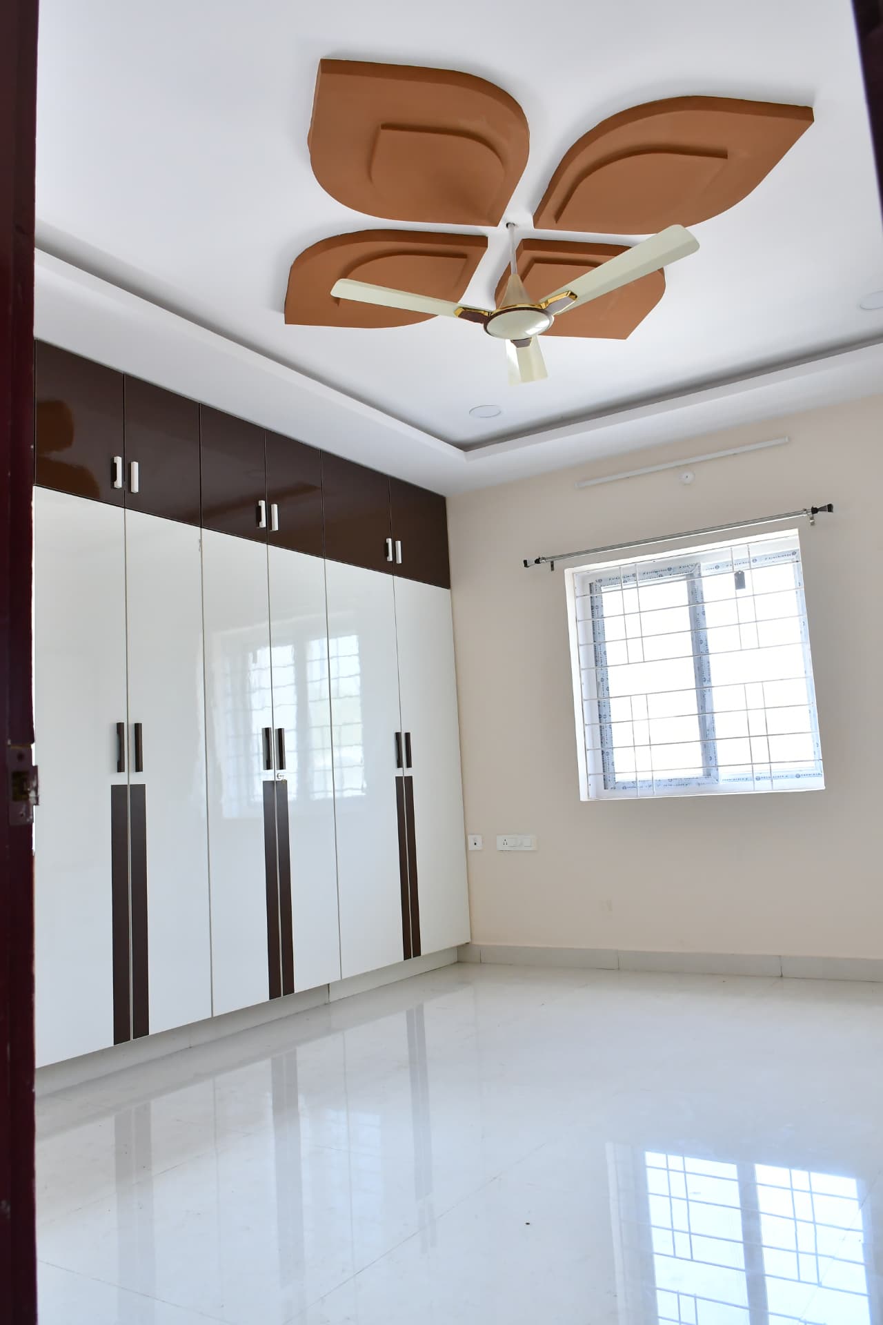 Mrs. Vasundara's Residence, Ballari — Glossy white and brown wardrobe with matching study ledge and dual windows