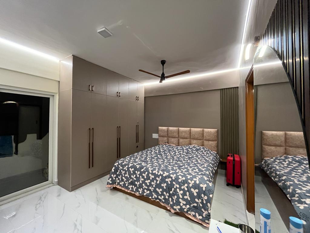 Rohan's Flat, Bangalore — Master bedroom with full-height mocha wardrobes, cushioned headboard and fluted panelling